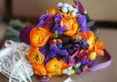 Bright orange and purple flowers in a bouquet with white lace