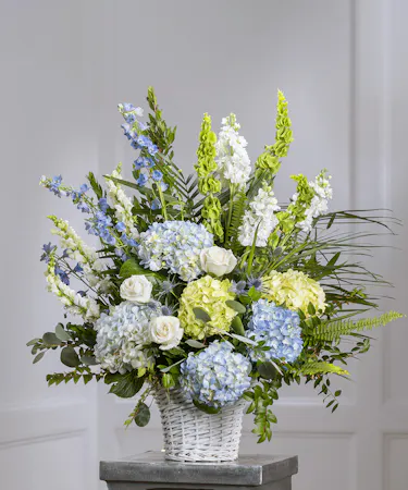 Blue & White Garden Sympathy Basket featuring hydrangea, delphinium, roses, stock and lush foliage
