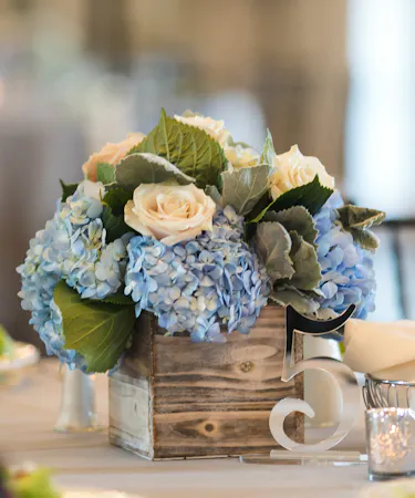 Blue and White Garden Table Centerpiece featuring blue hydrangea, white roses and dusty miller