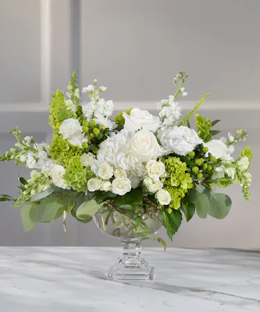 Table Centerpiece in glass pedestal container featuring white seasonal flowers