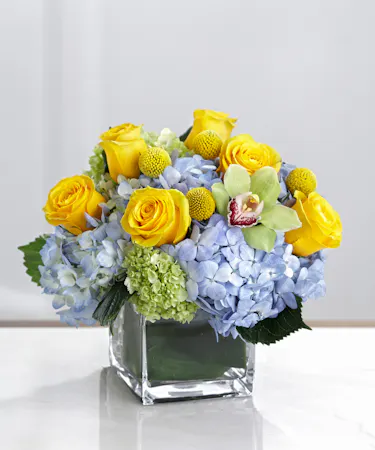 Blue Hydrangea, yellow roses, and orchids in a chic cube