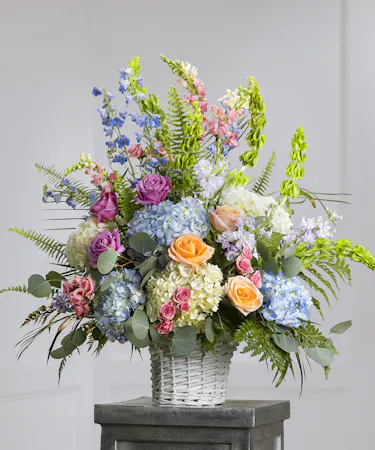 Pastel Garden Sympathy Basket featuring hydrangea, stock, snapdragons, delphinium, and orchids in a wicker basket