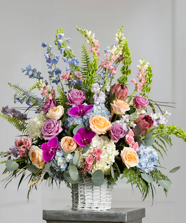 Pastel Garden Sympathy Basket featuring hydrangea, stock, snapdragons, delphinium, and orchids in a wicker basket