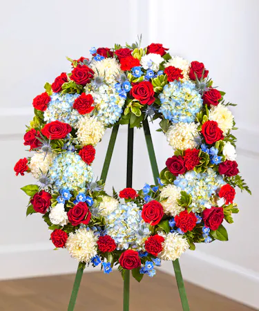 Patriot Garden Sympathy Wreath featuring hydrangea, roses, delphinium and foliage on a standing easel