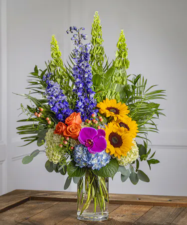 tall vibrant floral arrangement with sunflowers, orchids, roses, hydrangeas, and bells of ireland